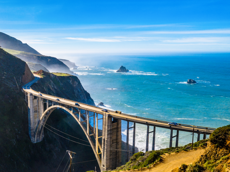 Cars traveling on a coastal viaduct, with the ocean in the background.