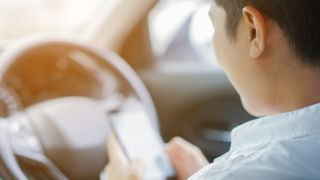 A man looks at his cell phone while sitting in the driver seat of his car.